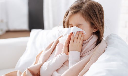 A child blowing her nose into a tissue, feeling unwell.